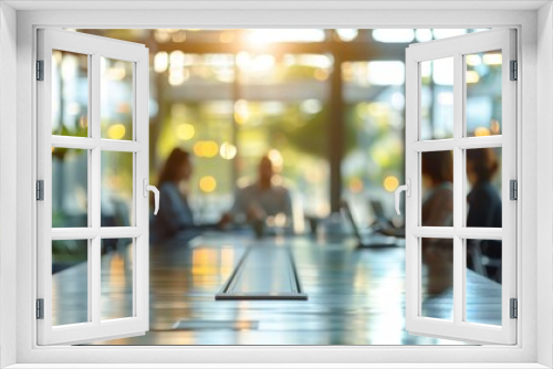 An out-of-focus view of a conference table with four people sitting around it in a brightly lit room. The table is made of wood and has a metal track down the center.