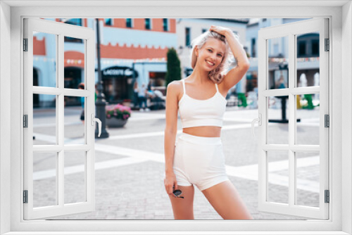 Young beautiful smiling female in trendy summer white cycling shorts and tank top clothes. Sexy carefree woman posing in street. Positive model . Cheerful and happy. Outdoors