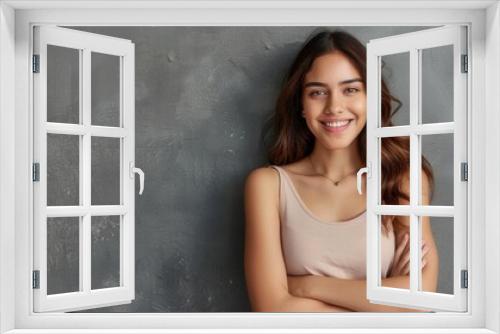 A young Hispanic woman with long brown hair and a pleasant smile stands with folded arms against a grey wall. Generative AI