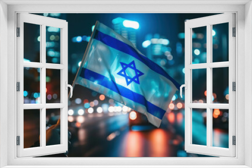 A hand holding an Israel flag with a blurred background of a city street.