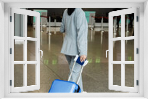 Traveler with luggage suitcase in the airport lobby before business trip. Woman with blue suitcase and phone is walking to the reception desk in the airport before flight departure.