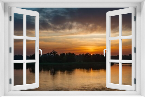 A tranquil sunset scene over a lake with a reflection of the sky and silhouette of trees, creating a serene and picturesque landscape