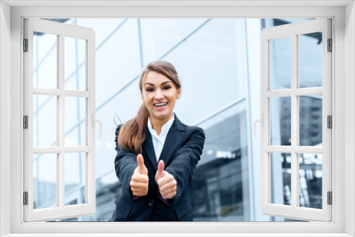 Successful young business woman showing thumbs up sign standing in front of his office.