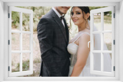 Handsome young groom in a suit and a bride in a white dress are hugging outdoors in the park. Photography, portrait of stylish newlyweds.