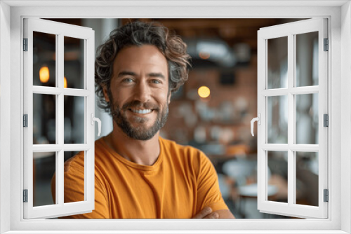 Smiling Man with Beard and Curly Hair in Orange T-Shirt Standing in Modern Office