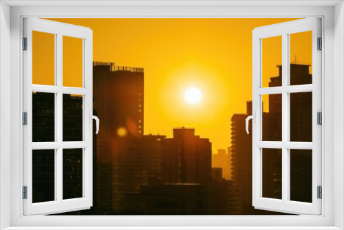 Silhouettes of skyscrapers against a vibrant orange sky, with the sun casting a warm glow over the urban landscape