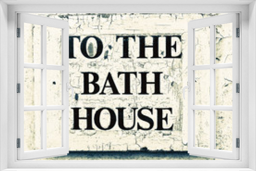 Fototapeta Naklejka Na Ścianę Okno 3D - A weathered sign on a white door with the words 'To the Bath House'.