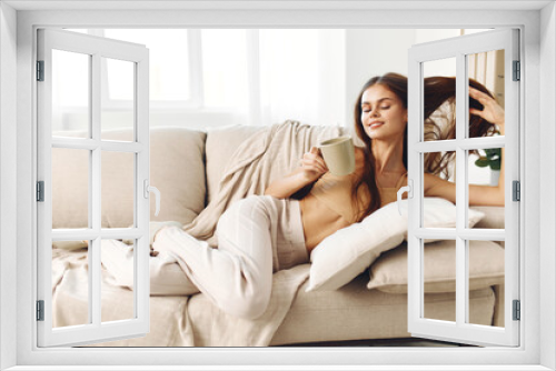 Cozy Morning Bliss: Smiling Woman Holding a Warm Coffee Mug on a Sofa with a Blanket in a Modern Home.