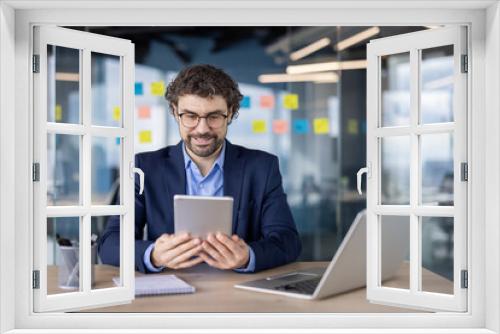 Business professional using digital tablet in modern office setting. Engaged in work activities surrounded by modern decor, sticky notes, laptop, and notepad, conveying productivity