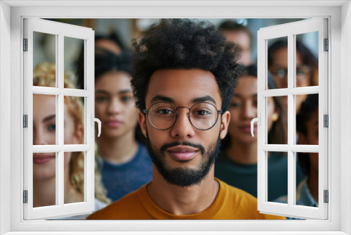 Diverse group of young adults standing together, showing unity and strength. Focus on a man with glasses in the front, smiling confidently.