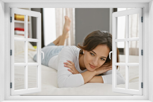 Relaxed hispanic woman lying on bed in a cozy bedroom, looking at the camera with a gentle smile.