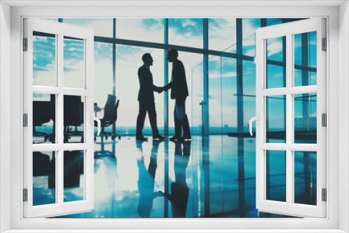 Silhouettes of businessmen shaking hands in glass office.