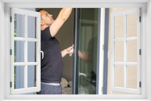 Young man cleans the windows in the house. He splashes detergent, rubs and removes water at the glass