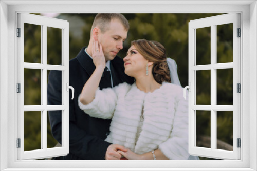 A bride and groom are posing for a picture in the snow. The bride is wearing a white coat and the groom is wearing a black suit. They are both smiling and looking at the camera