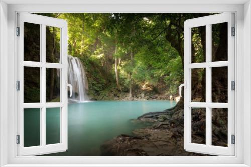 Fototapeta Naklejka Na Ścianę Okno 3D - Sunlight beams and rays shine through leaves of trees in tropical rainforest park in Thailand with beautiful waterfall falling in clear pond and old big tree on foreground